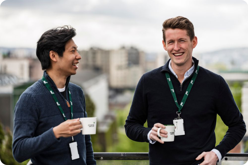 To ansatte på terassen smiler med Athene Group kaffekopper og nøkkelkort